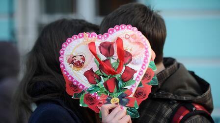 Влюбленная пара целуется, закрыв лицо валентинкой